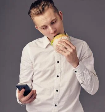 Man eat hamburger in cafe while watch video on his phone Stock Photos