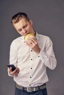 Man eat hamburger in cafe while watch video on his phone Stock Photos