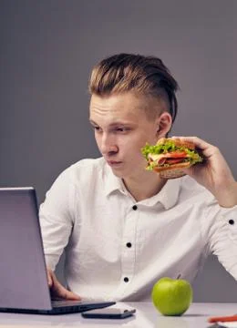 Man eat hamburger in office while watch video on his laptop Stock Photos