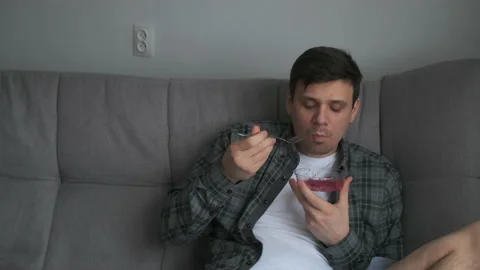 Man is eating beetroot salad from plastic container sitting on couch at home. Stock-Footage 158310846