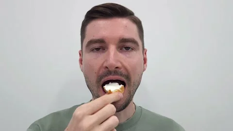 Man eating a bite-sized snack with white cream on a plain background Stock Footage 284043805