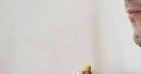 Man is eating burger at light background, mouth closeup, side view. Stock Footage 108018989
