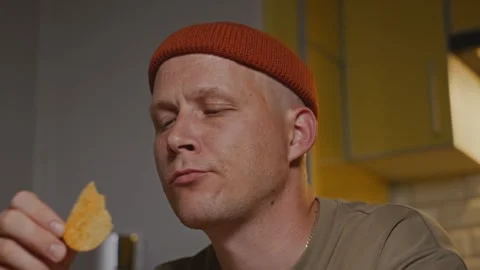 Man eating chips at kitchen table in calm evening light Stock Footage 317991990