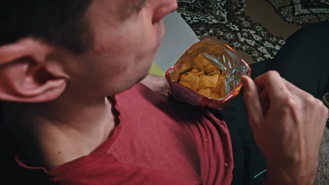 Man is Eating Crispy Potato Chips in a Package on the Sofa Stock Footage 260542760