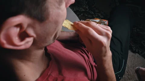 Man is Eating Crispy Potato Chips in a Package on the Sofa Stock Footage 260805300