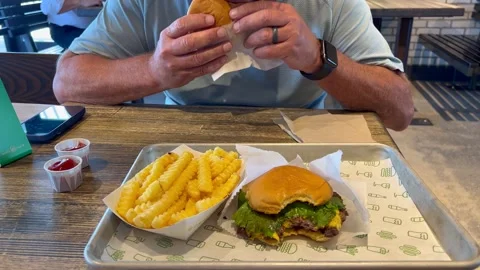 A man eating a delicious Shake Shack burger, chicken sandwich, and French f.. Stock Footage 262550041