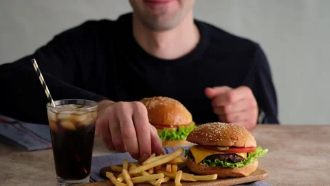 Man eating Fast food. Burgers, french fries, cola. A woman made a hamburger from Stock Footage