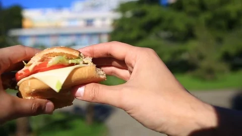 A man is eating fast food on the street. He wears a hamburger and eats it Stock Footage