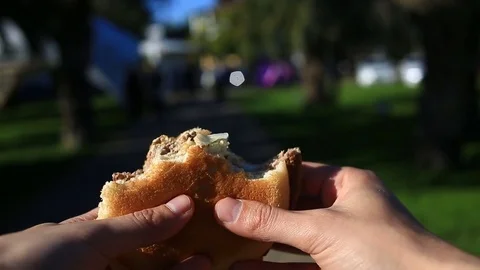 A man is eating fast food on the street. He wears a hamburger and eats it Stock Footage