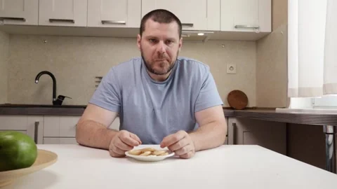 Man Eating Fresh dry Bread rings, sitting at a table in a casual kitchen, e.. Stock Footage 300085672