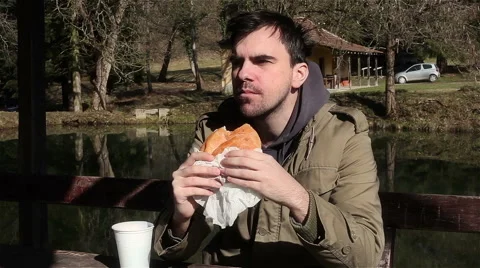 Man eating hamburger and drinking water in park. Fast food. Sandwich. Obesity. Stock Footage 47445159