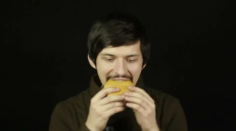 Man eating a hamburger on a black background  Stock Footage 25107594