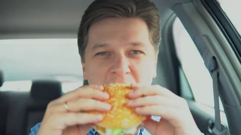 A man is eating a hamburger in a car. Stock Footage 81815425