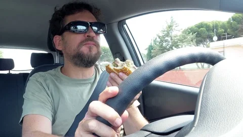 Man eating hamburger while driving car closeup Video stock 77621169