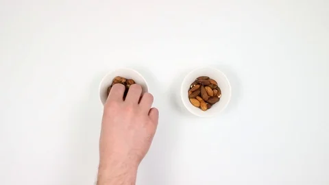 The man is eating nuts. Almonds and hazelnuts. Nuts on a white table. Stock-Footage 88399285