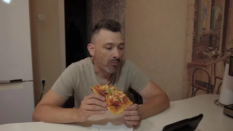 Man eating pizza and glancing at tablet on table Stock Footage 341832834