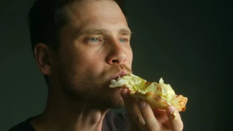 Man eating pizza slice with lettuce on dark background Stock Footage 313233752