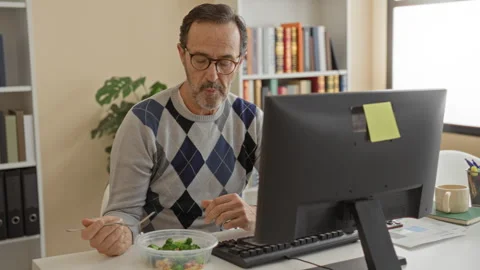 Man eating salad at computer in building, fork raised to mouth, hands visib.. Stock Footage 337443601