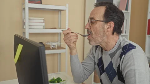 Man eating salad with fork, holding clear plastic container beside keyboard.. Stock Footage 337442146