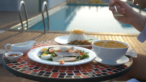 The man is eating Tom Yam at a table by the pool Stock Footage 86537077