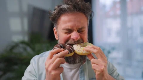 A man eating two donuts with pleasure and at the same time. Binge eating concept Stock Footage 342957481