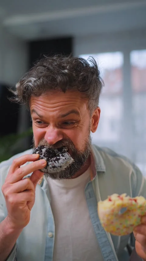 A man eating two donuts simultaneously with delight. Sugar addiction. Slow Stock Footage 346728572