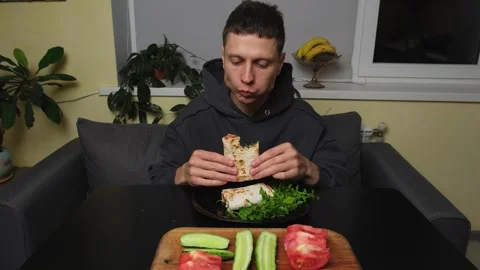 Man eating vegetable lavash wrap with cheese and greens in everyday home kitchen Stock Footage 316471272