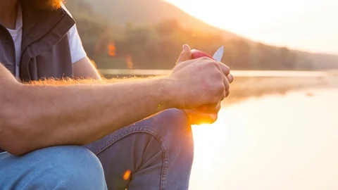A man eats an apple sitting on the shore of a reservoir at sunset Stockbeeldmateriaal 81429975