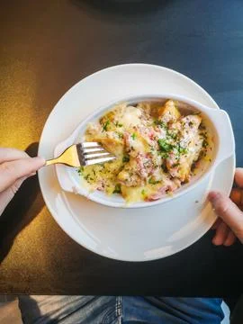 A man eats baked dumplings with a sauce of bacon, ham, herbs and cheese. Stock Photos
