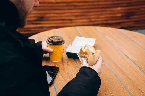 A man eats a burger and drinks coffee while sitting at a fast food cafe table. Stock Photos