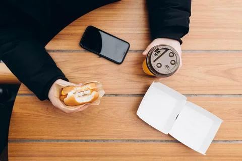 A man eats a burger and drinks coffee while sitting at a fast food cafe table. Stock Photos