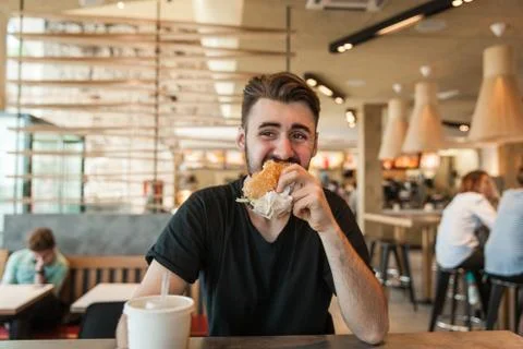 A man eats a burger at dinner in a cafe. Stock Photos