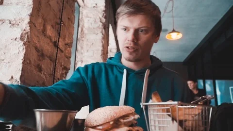 A man eats, burgers at a table in a cafe Stock Footage 87285585
