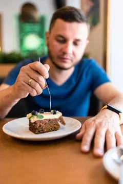 A man eats a cake with blueberries in a cafe. Stock Photos