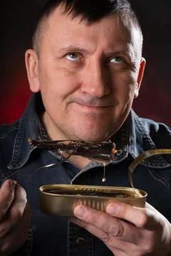 Man eats canned fish with a fork. Pleasant emotions on my face. Stock Photos