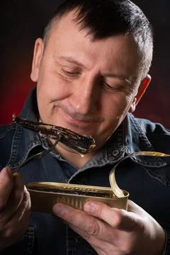 Man eats canned fish with a fork. Pleasant emotions on my face. Foto stock