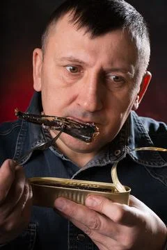 Man eats canned fish with a fork. Pleasant emotions on my face. Stock Photos
