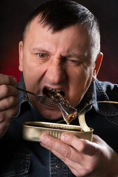 Man eats canned fish with a fork. Pleasant emotions on my face. Stock Photos