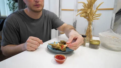 A man eats chicken wings in slow motion. Eat meat with ketchup in the apartments Stock Footage 293845969