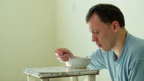A man eats Chinese noodles while sitting on the floor behind an old dirty stool Stock Footage 131963859