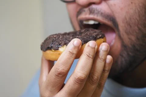 Man eats chocolate sprinkle doughnut with enthusiasm Stock Photos