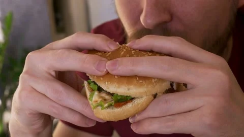 Man eats a delicious hamburger with white bun and chicken fillet. Poor nutrition Stock Footage 168762786