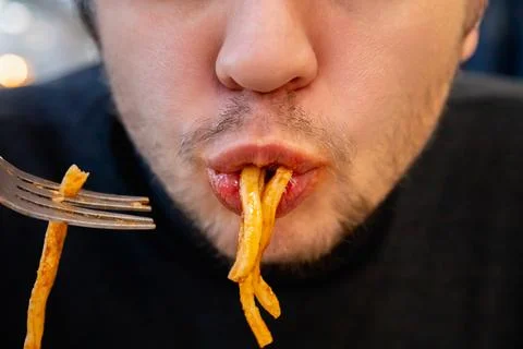 Man eats fat pasta, sucks it with his mouth showcasing overeating Stock Photos