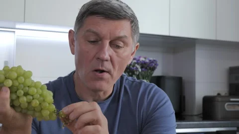 A man eats grapes in his kitchen Video stock 324712064