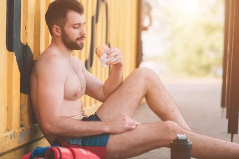 Man eats a hamburger after a workout. Very hungry, fatty and unhealthy food. Fotos Stock