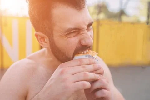 Man eats a hamburger after a workout. Very hungry, fatty and unhealthy food. Foto stock