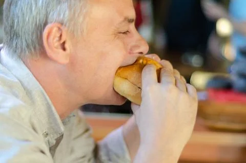 The man eats hamburger with pleasure. Stock Photos