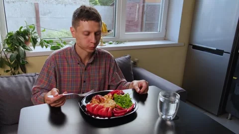 A man eats homemade pasta with vegetables at home in the kitchen. Video stock 316408234