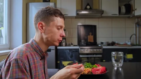 A man eats homemade pasta with vegetables and arugula at home in the kitchen. Stock-Footage 316408400