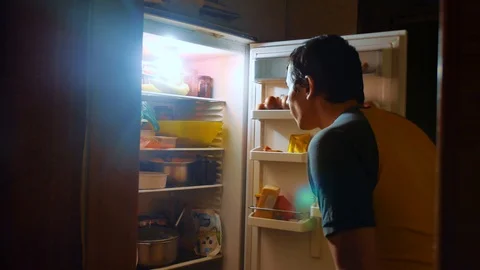 Man eats hunger and gluttony from the refrigerator at night. man looks into the Stock Footage 97964559
